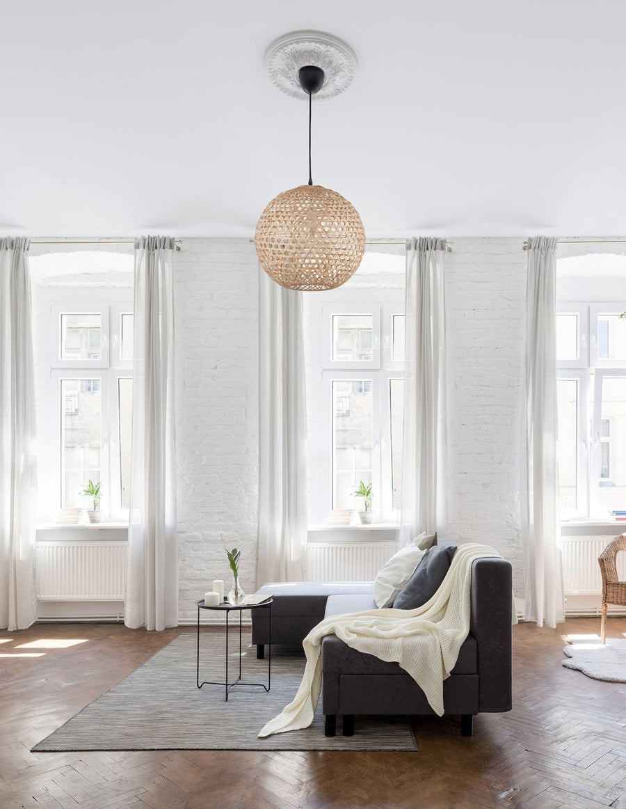 Suspension en rotin tressé suspendue au-dessus d'un salon blanc baigné de lumière