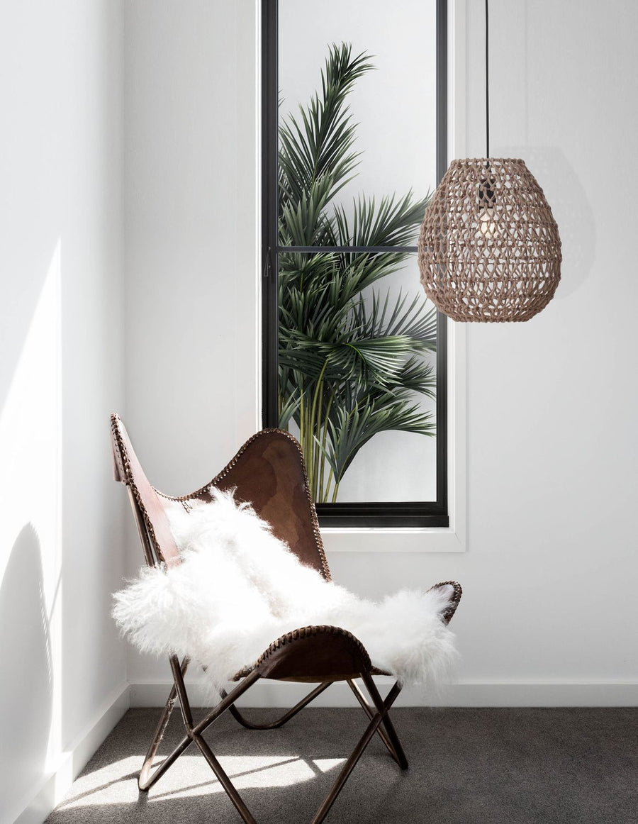 Suspension en rotin tressé suspendue dans un intérieur blanc avec fauteuil en cuir et peau de mouton