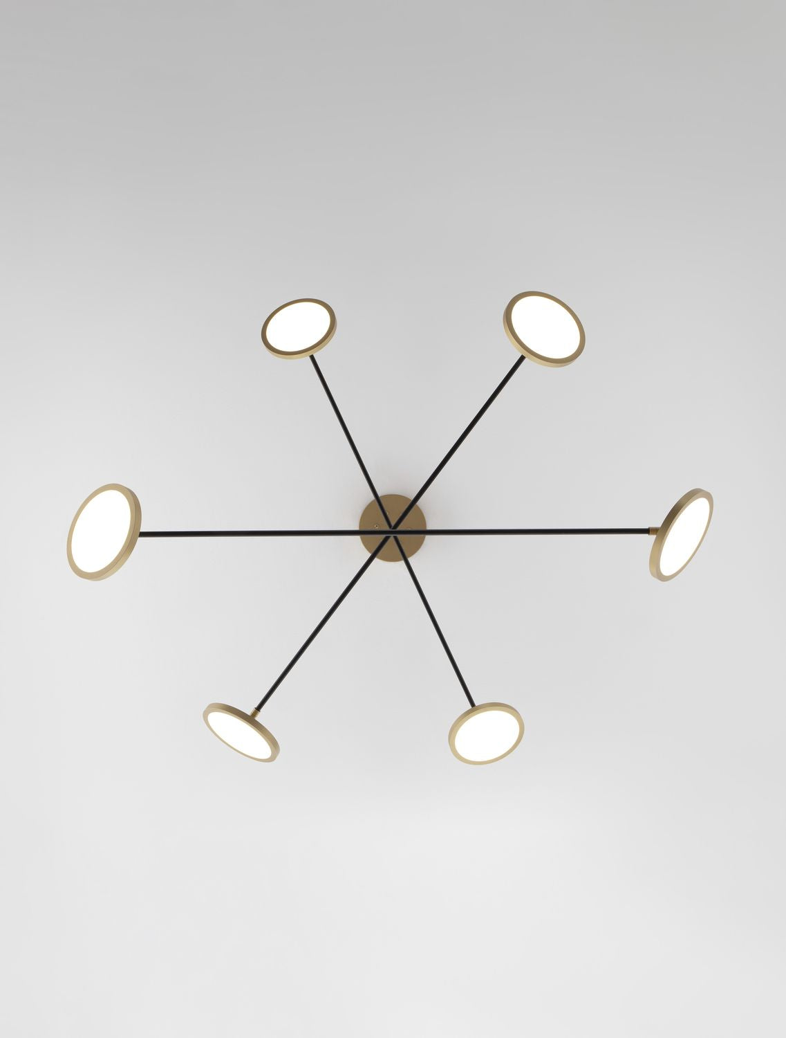 Vue de dessous du luminaire, montrant six bras noirs rayonnant et disques lumineux.