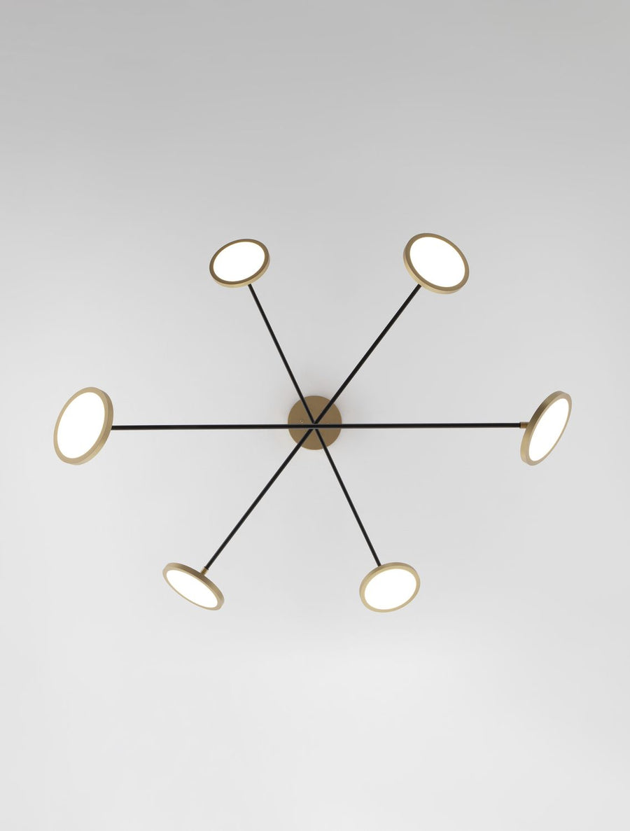 Vue de dessous du luminaire, montrant six bras noirs rayonnant et disques lumineux.