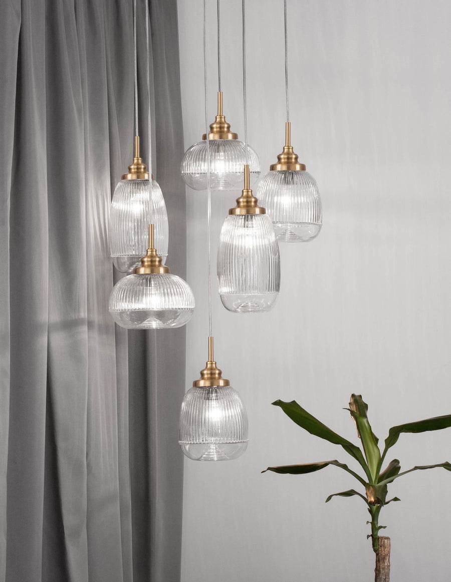 Suspension dorée à six lumières en verre cannelé devant un rideau gris
