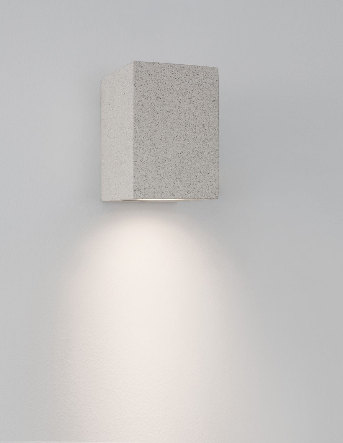 Luminaire mural allumé projetant une lumière chaude en cône sur le mur