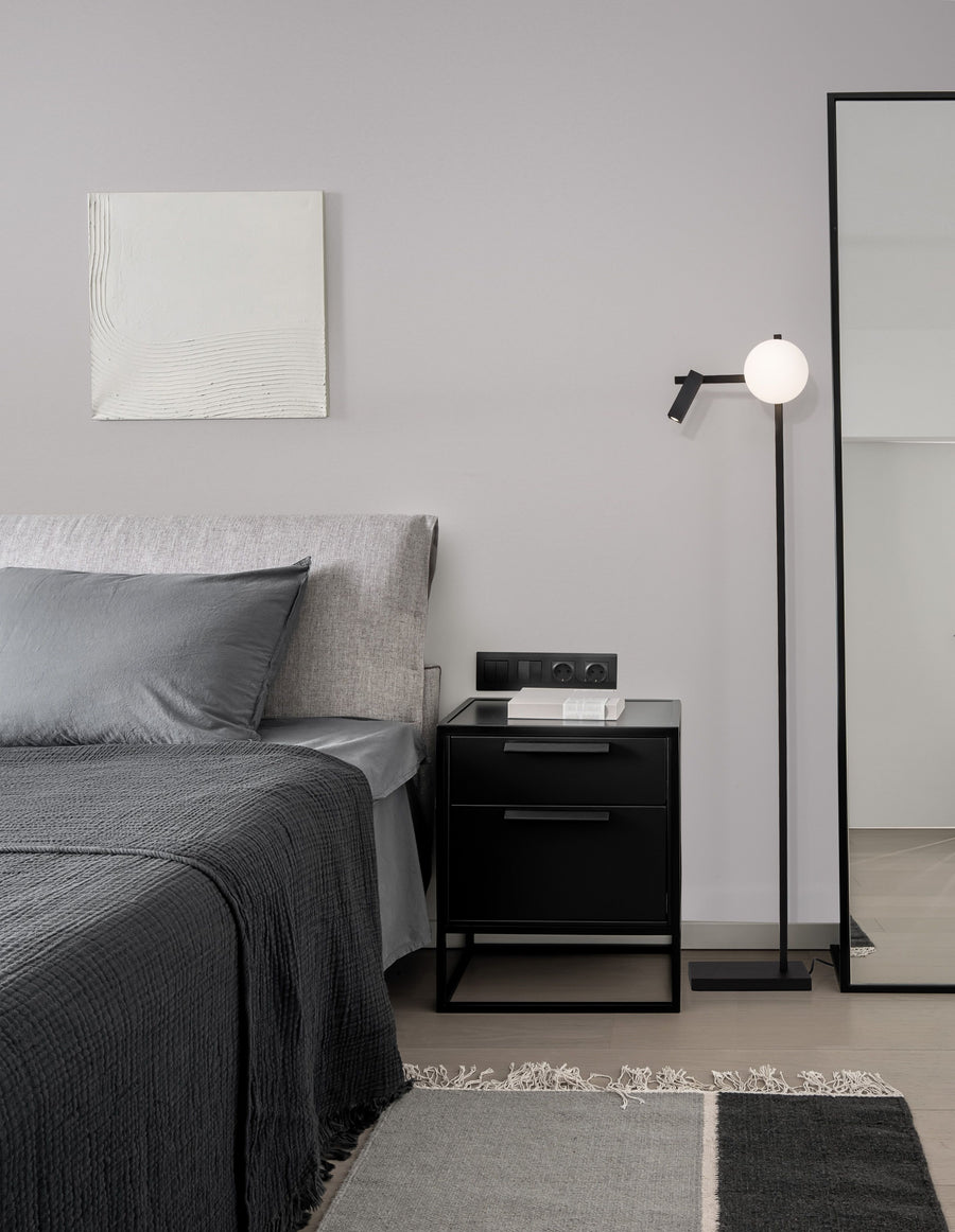 Lampadaire noir installé près d'un lit, dans une chambre grise et minimaliste