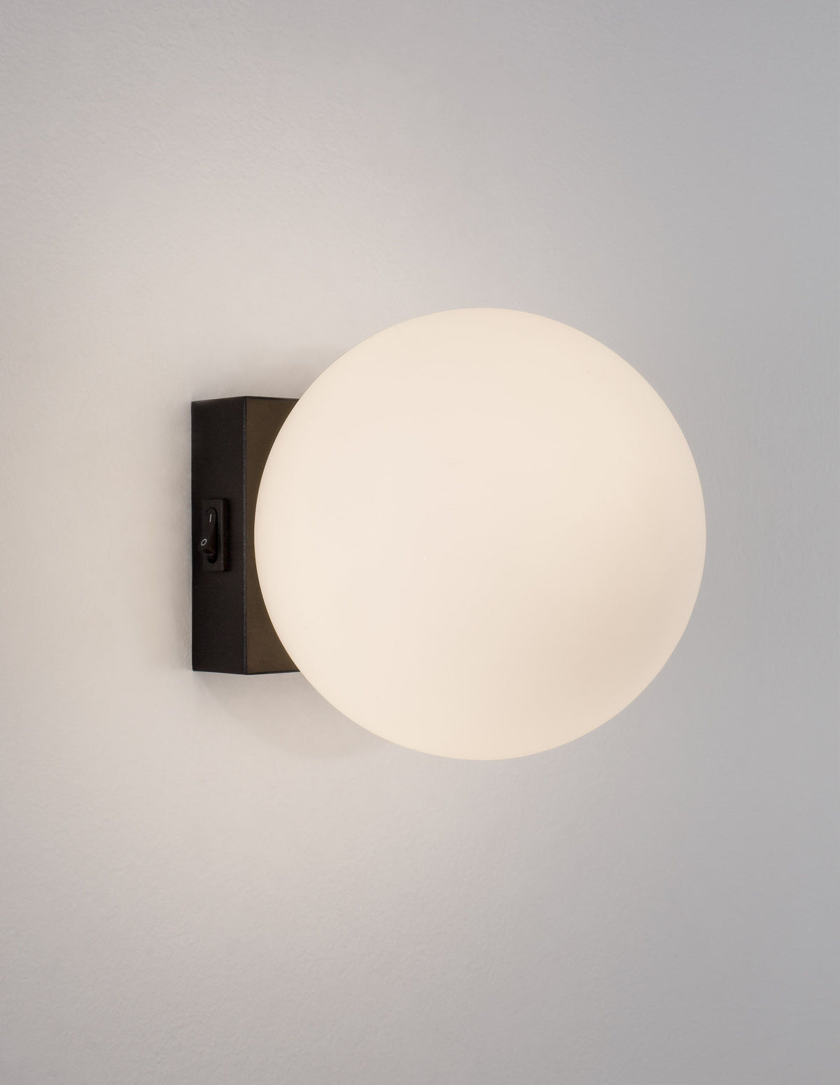Applique murale allumée, globe en verre opalin diffusant une lumière chaude.
