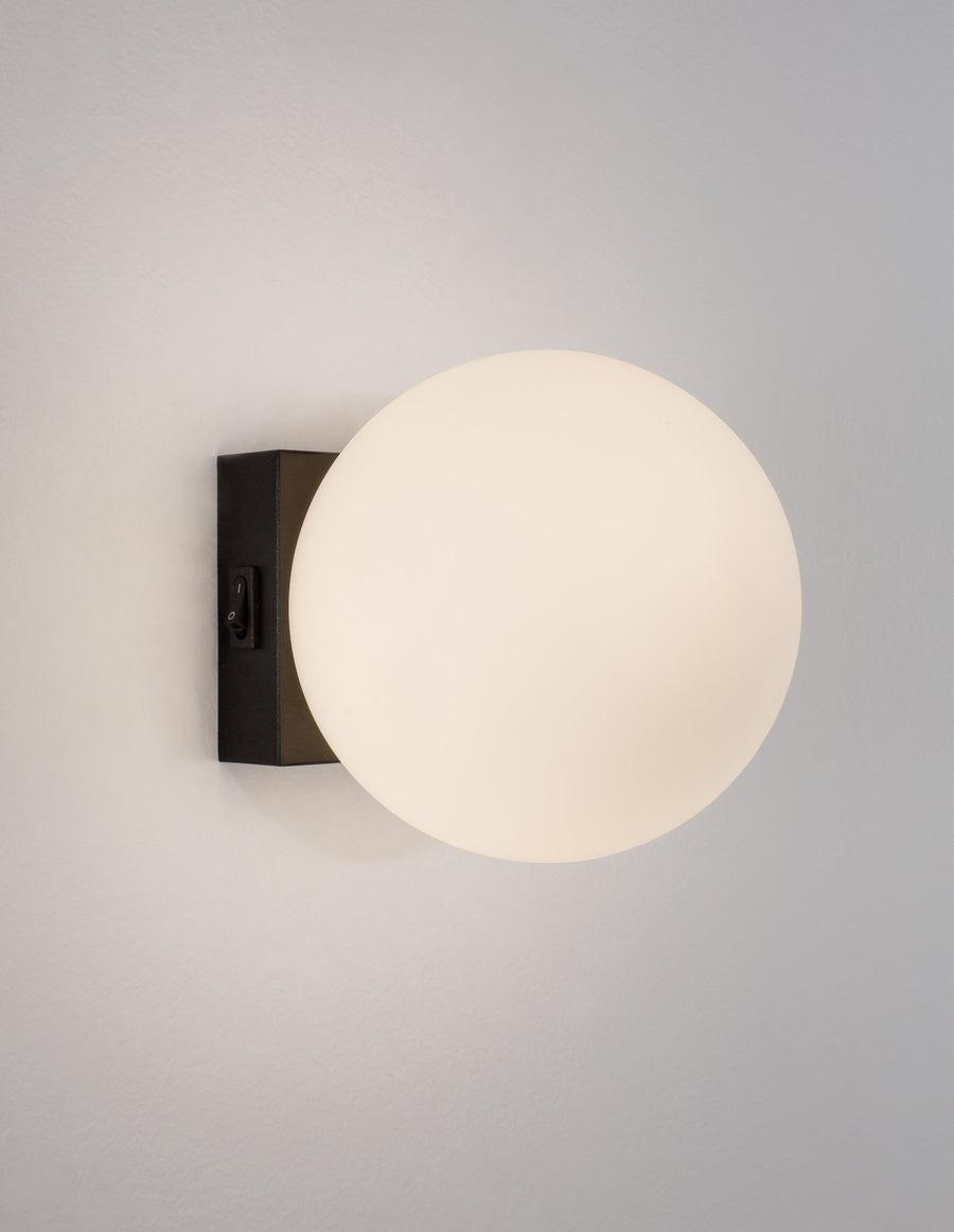 Applique murale allumée, globe en verre opalin diffusant une lumière chaude.