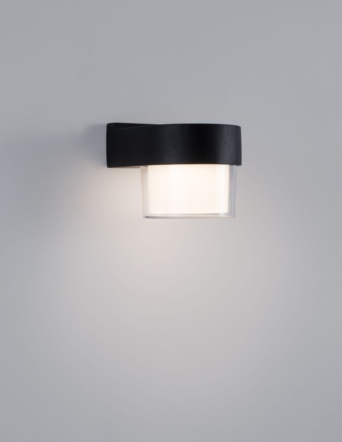 Applique murale allumée sur mur gris, halo lumineux doux et capot noir