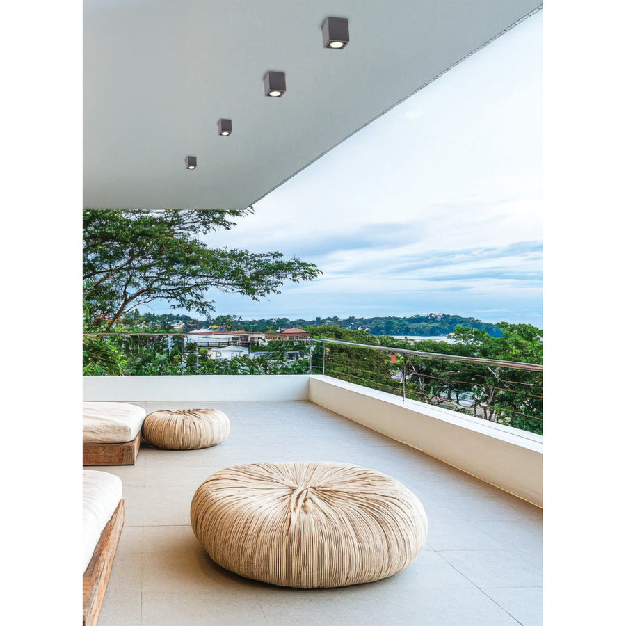 Quatre plafonniers cubiques gris sous une terrasse extérieure avec poufs