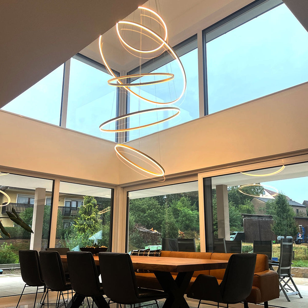 Salle à manger sous verrière avec anneaux dorés suspendus et vue sur le jardin