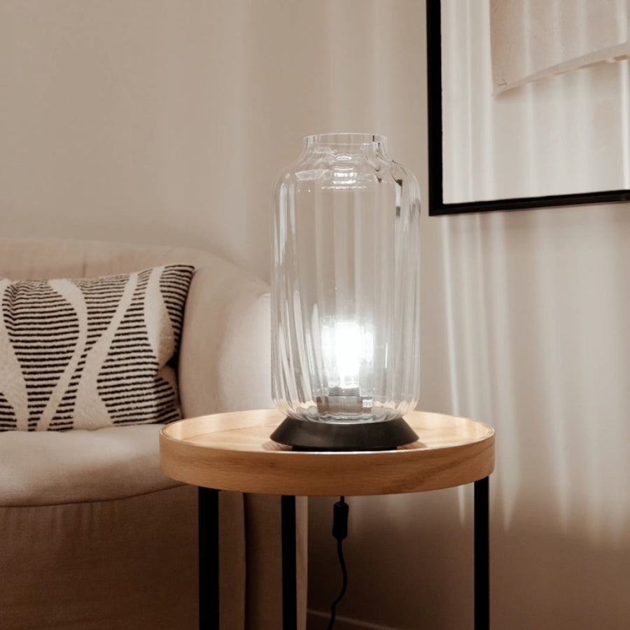 Lampe transparente posée sur une table ronde, près d'un canapé et d'un coussin rayé