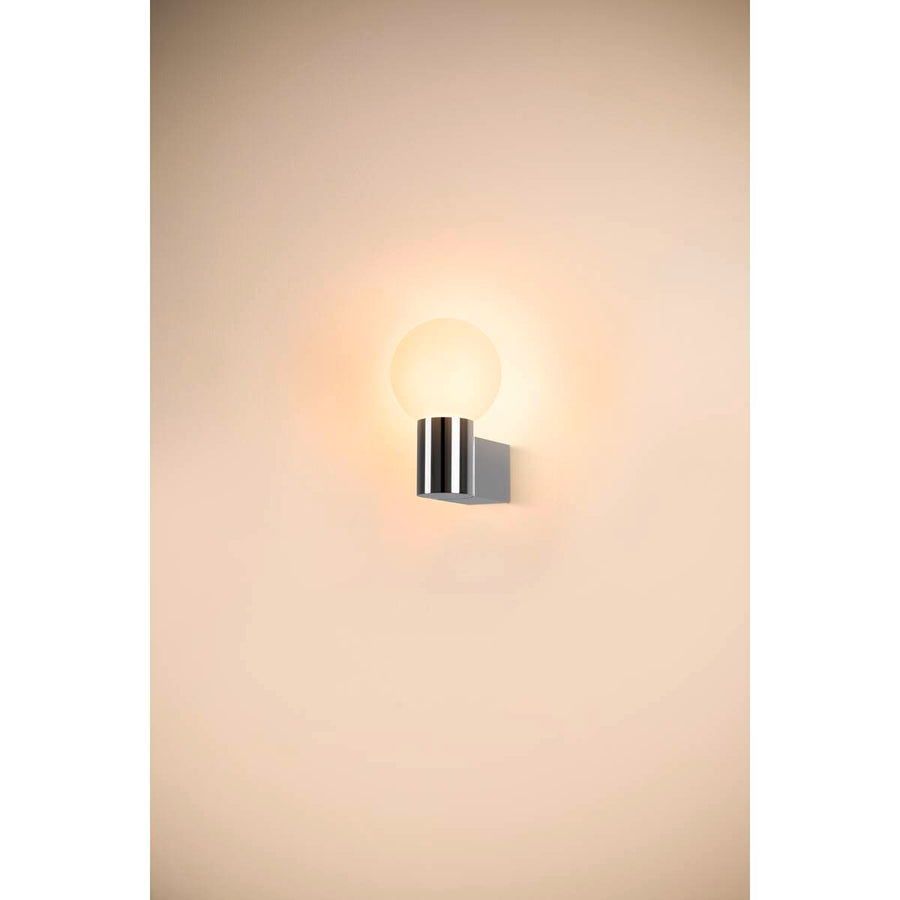 Applique murale allumée fixée sur un mur beige, diffusant une lumière chaude