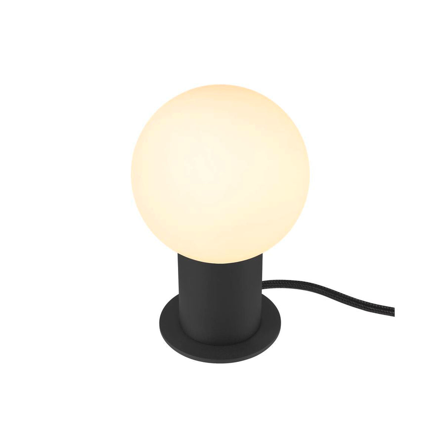 Lampe à poser noire surmontée d'un globe blanc allumé, vue de face