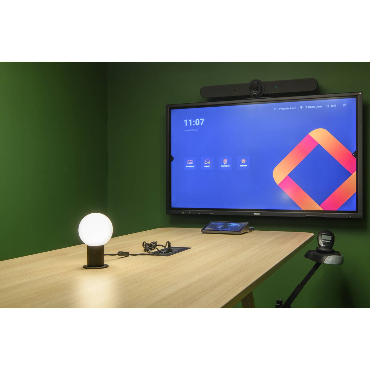 Lampe posée sur un bureau devant un grand écran, pièce verte