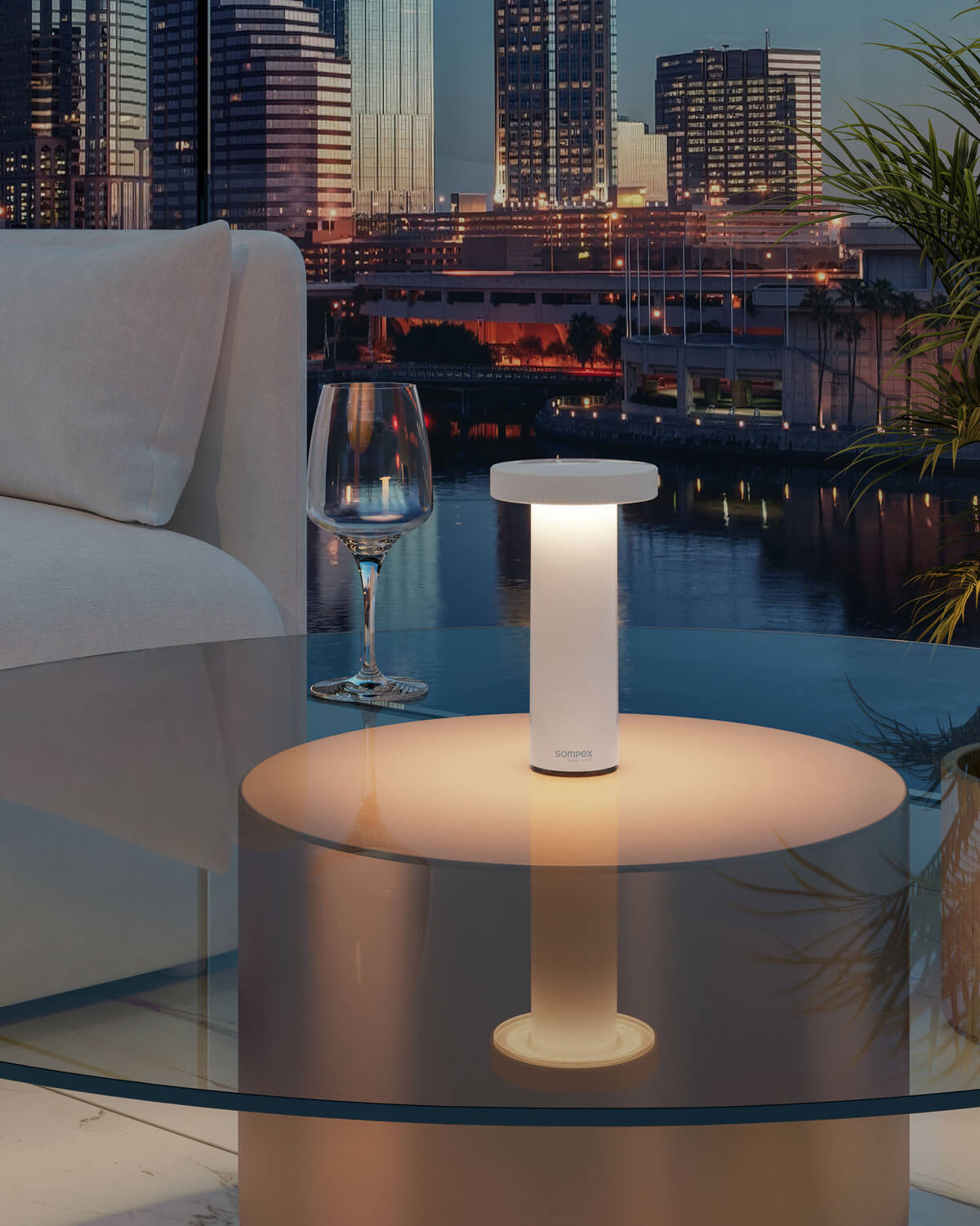 Lampe blanche allumée posée sur table en verre, terrasse urbaine au crépuscule