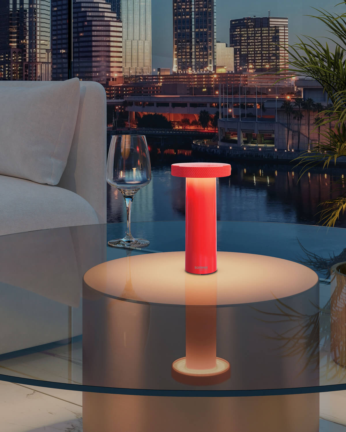 Lampe nomade posée sur table basse en verre devant une vue nocturne urbaine