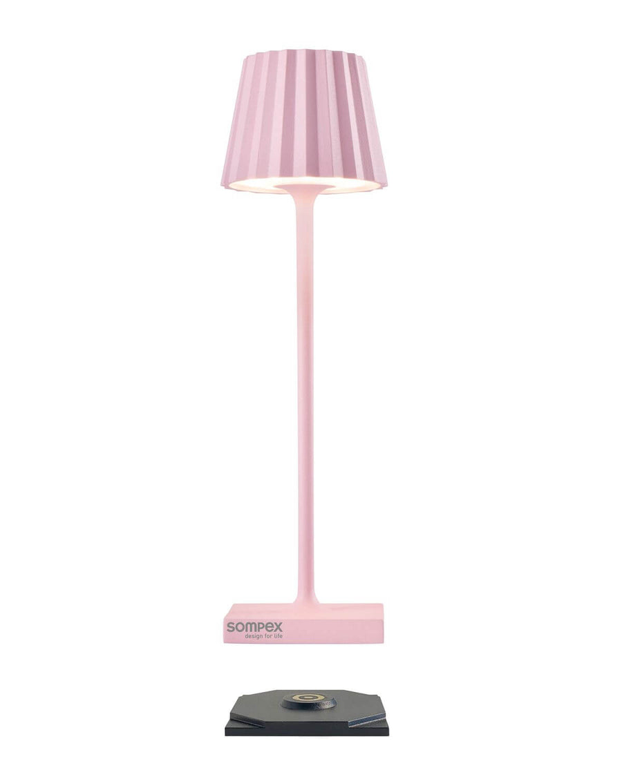 Lampe rose avec socle de recharge noir séparé, présentée de face sur fond blanc.