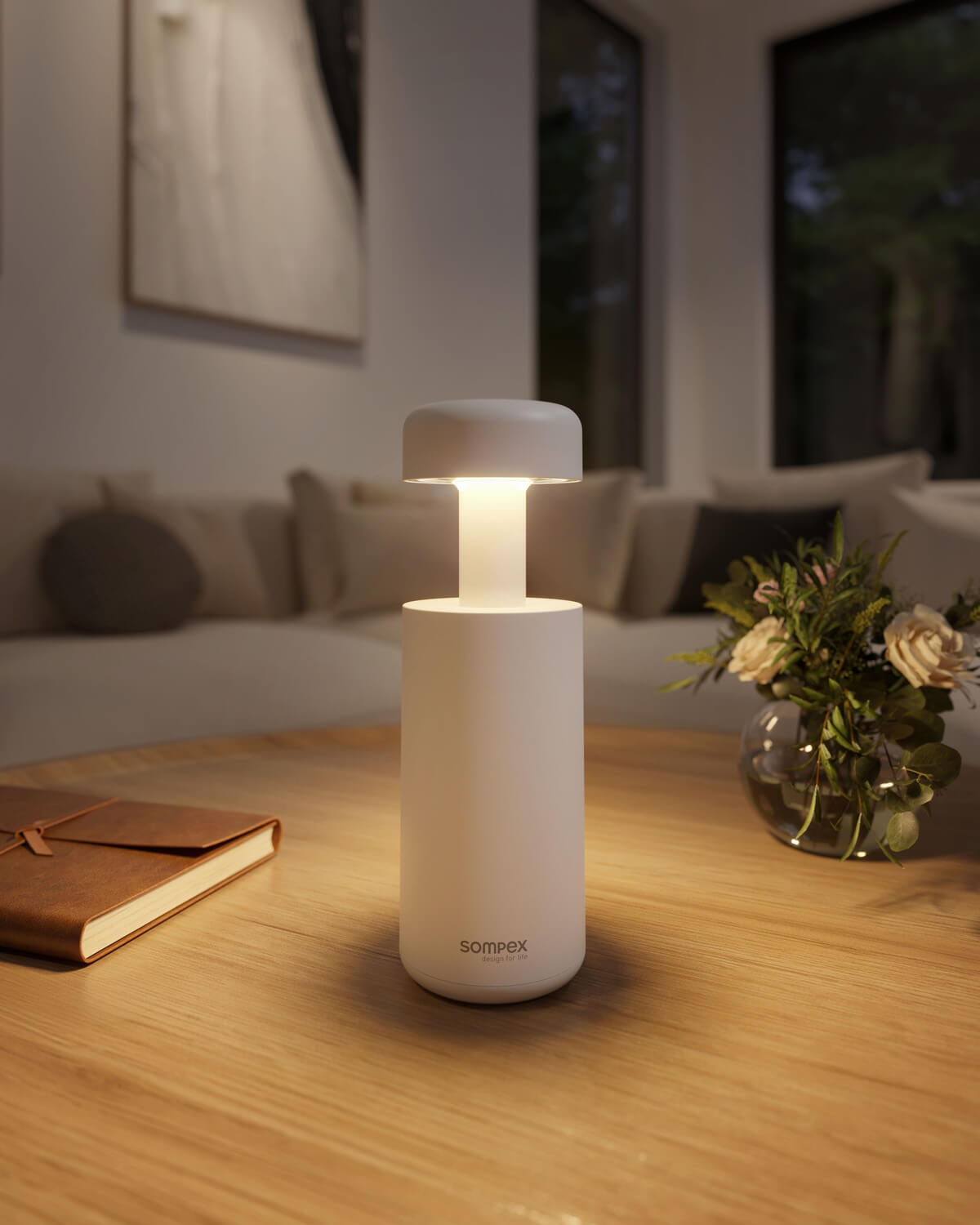 Gros plan de la lampe allumée sur table en bois, avec carnet et fleurs.