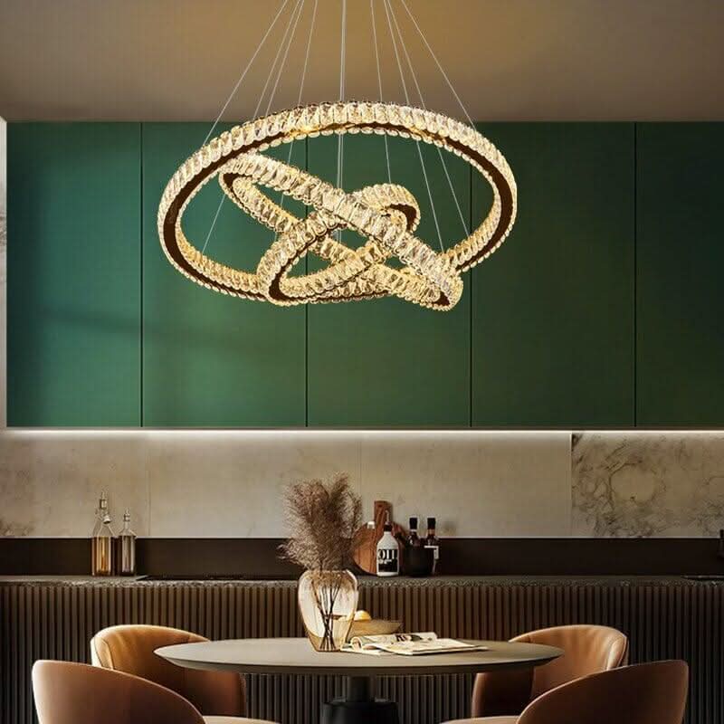 Suspension dorée à anneaux noués éclairant une table ronde devant un mur vert