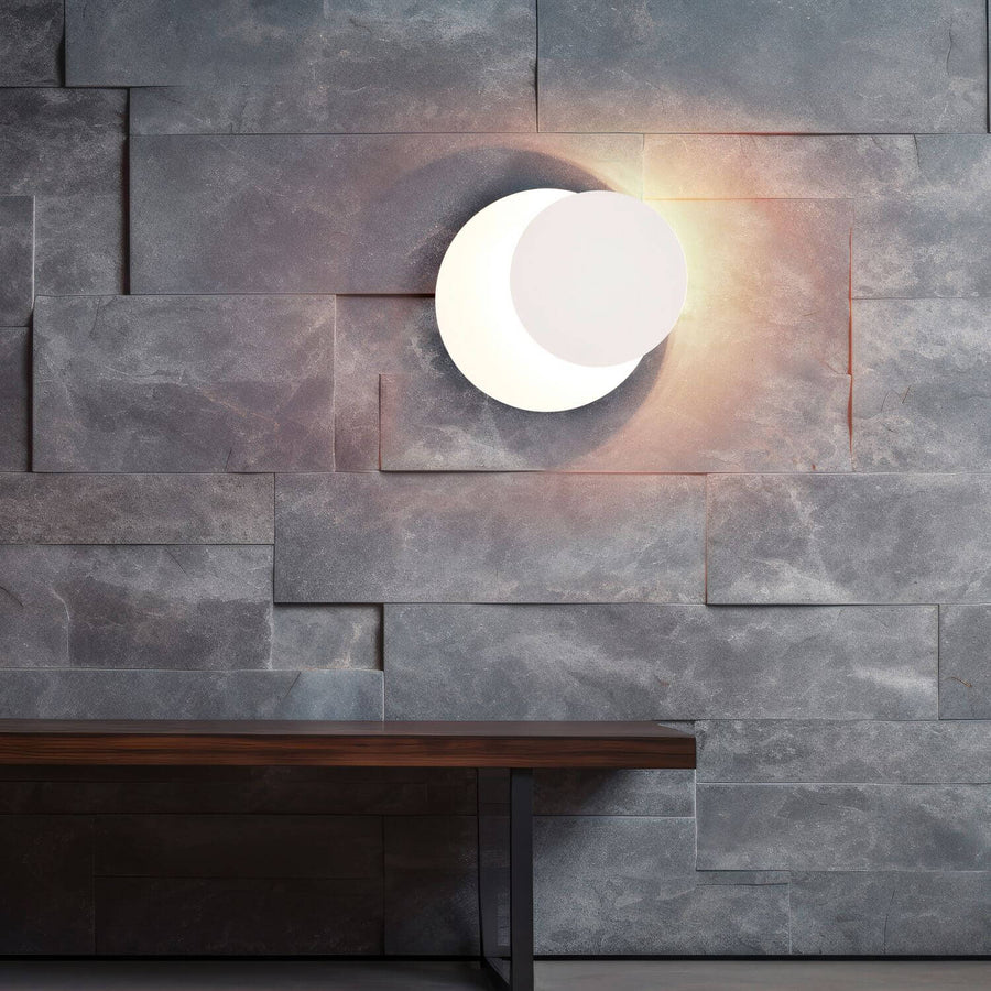 Applique murale blanche allumée sur un mur de pierre grise, au-dessus d'une table en bois