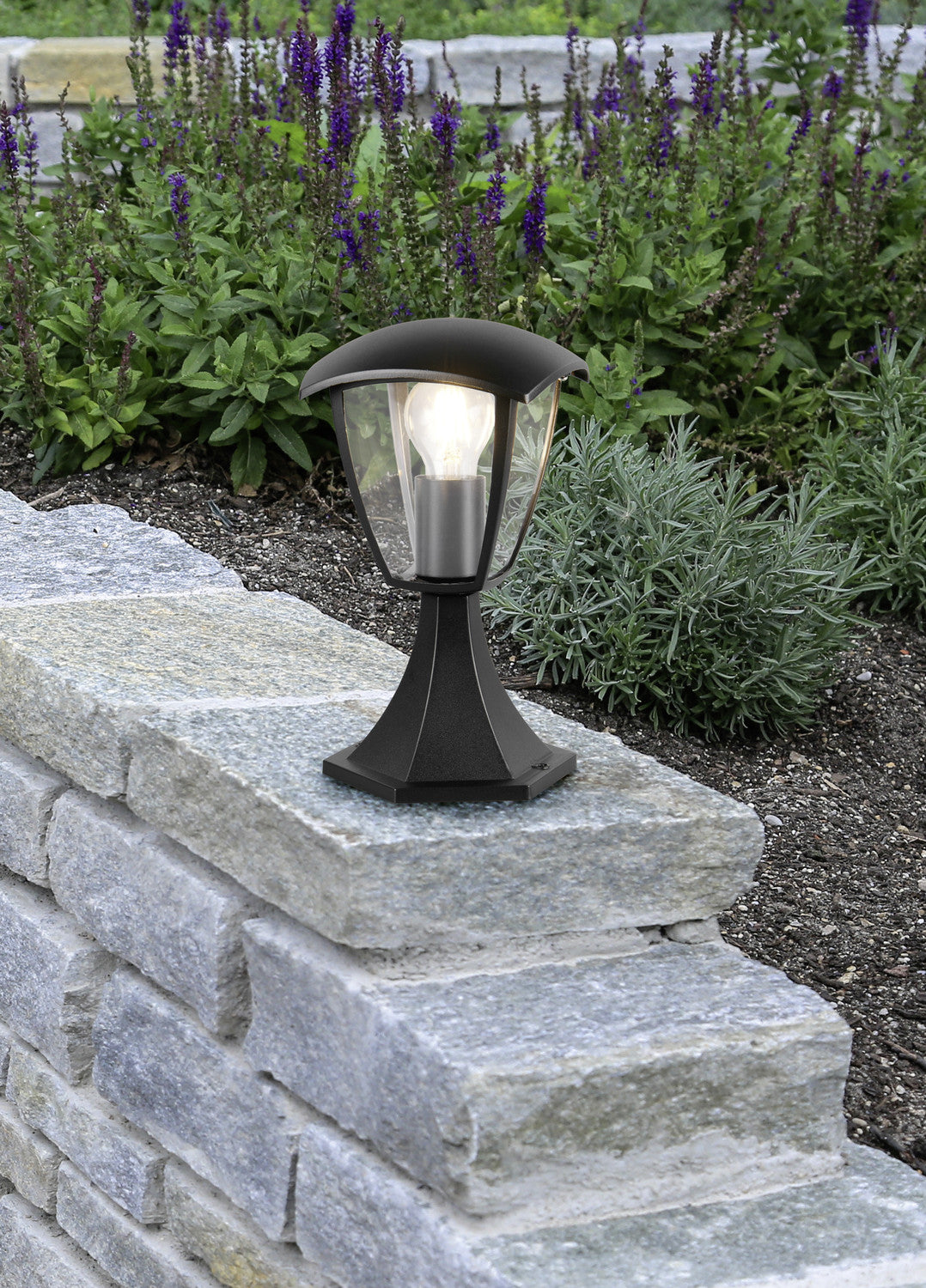 Luminaire extérieur noir installé sur un muret en pierre dans un jardin fleuri
