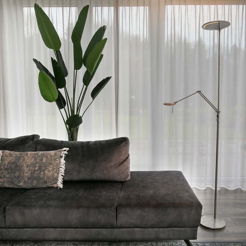 Mise en ambiance salon, lampadaire allumé près d'un canapé gris et d'une plante.