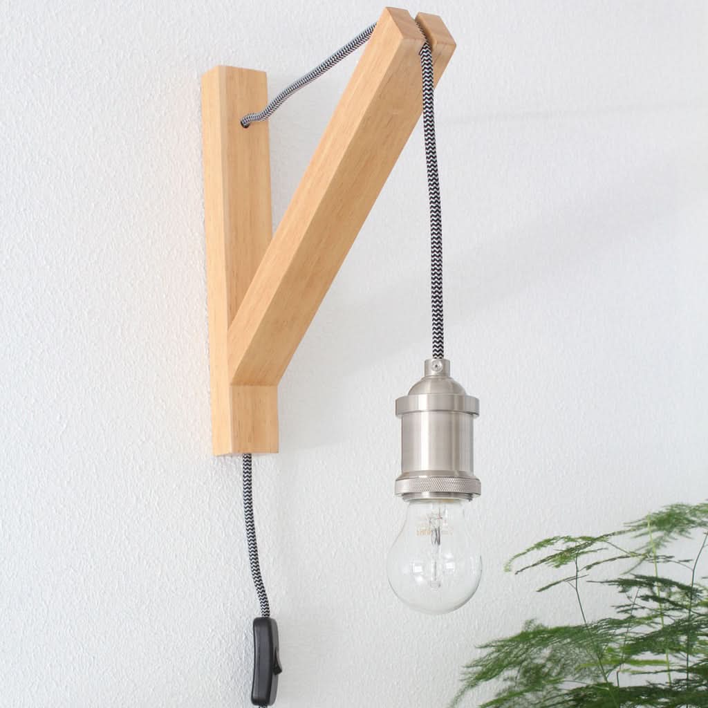 Applique murale installée sur un mur blanc, avec interrupteur tirette et plante verte.