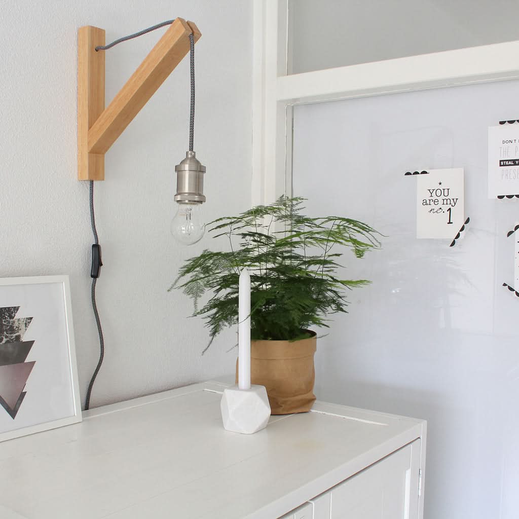 Mise en ambiance sur meuble blanc avec cadre photo, plante et lampe murale non allumée.