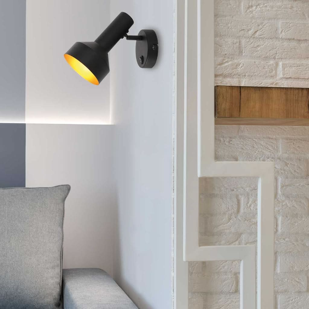 Mise en ambiance : applique allumée près d'un canapé gris devant mur de briques