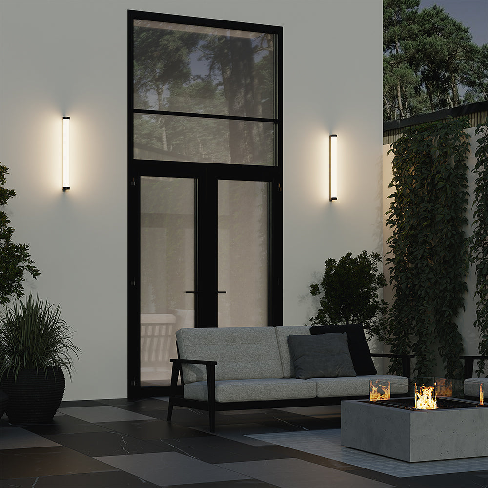 Mise en ambiance nocturne sur une terrasse avec deux appliques allumées et feu de jardin.