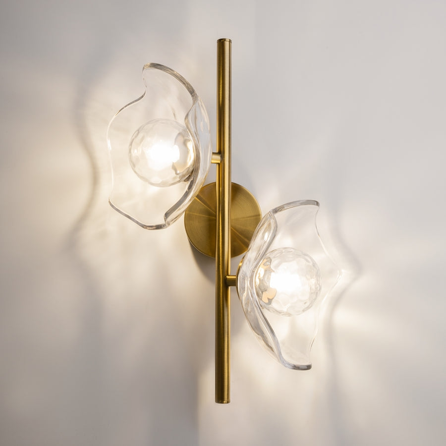 Applique murale dorée installée au mur, deux globes en verre transparent éclairés, ombres portées.