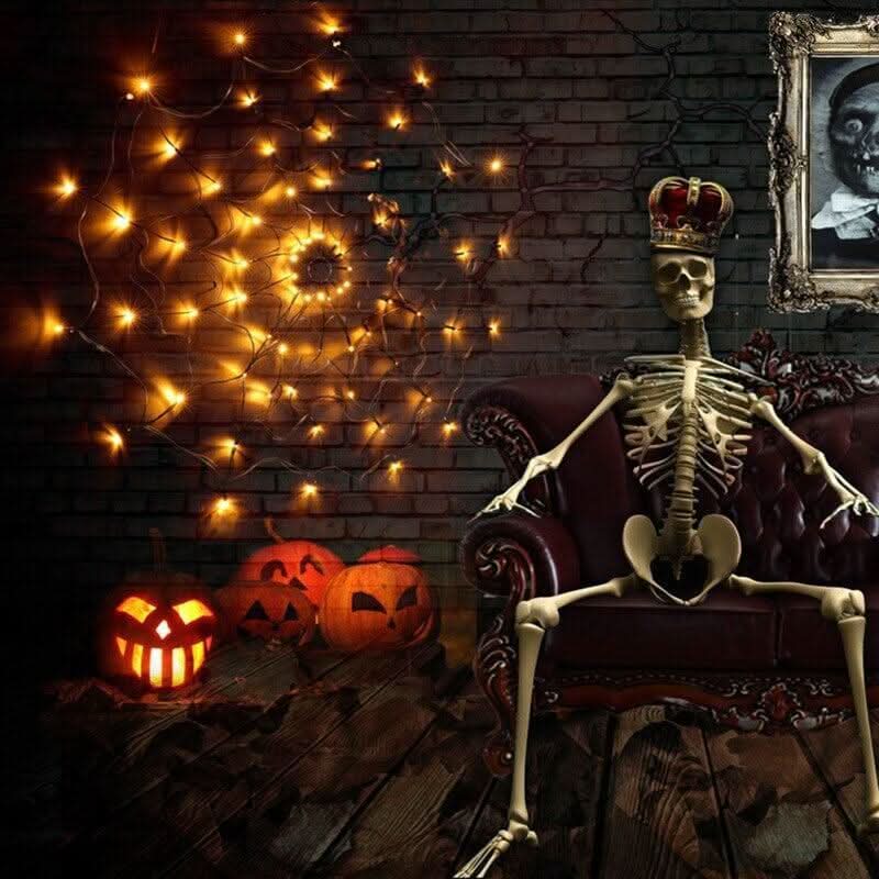 Mise en ambiance Halloween : toile lumineuse dorée sur mur de briques, squelette couronné dans un fauteuil